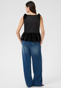 Haut noir avec des nœuds en tissu bouffant aux épaules, taille peplum en velours doux, associé à un jean en denim bleu délavé à jambe large.