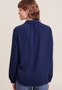 Marineblauw overhemd met lange mouwen van een gestructureerde stof, met een kraag en een plooitje aan de achterkant. Voorzien van geknoopte manchetten en een ontspannen pasvorm.