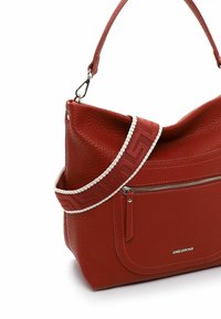 Sac à main en cuir texturé rouge avec une poche zippée à l'avant et une bandoulière en tissu à motifs avec des accents blancs.
