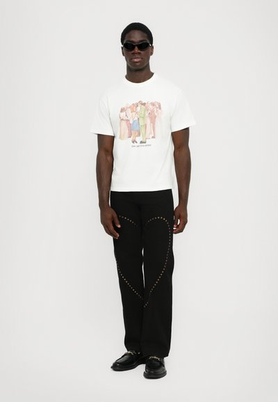 T-shirt graphique blanc mettant en avant une illustration colorée, associé à un pantalon noir orné d'embellissements en forme d'étoiles dorées le long des coutures.