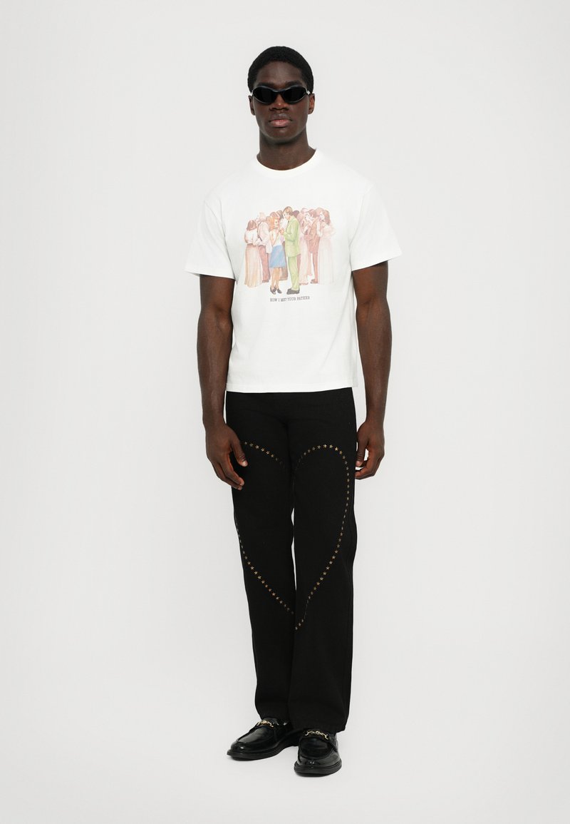 White graphic t-shirt featuring a colorful illustration, paired with black pants adorned with gold star embellishments along the seams.