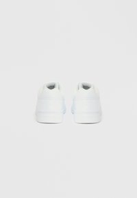 Λευκά αθλητικά παπούτσια με λείο δερμάτινο φινίρισμα, επενδυμένο περιλαίμιο και υφή από καουτσούκ στη σόλα. Μινιμαλιστικός σχεδιασμός με διακριτικό ανάγλυφο λογότυπο στη φτέρνα.