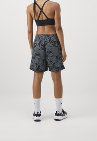 Brassière de sport noire avec bretelles croisées, associée à un short noir avec un motif texturé. Chaussettes blanches aux chevilles et chaussures de sport noires.