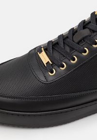 Svart sneaker med nätstruktur och slät läder. Guldiga detaljer och svarta snören. Smidig, rund form med platt sula.