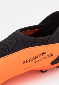 Musta ja oranssi jalkapallokenkä, jossa on teksturoitu pinta, korkeavartinen muotoilu ja näkyvät brändäykset, joissa lukee "Predator" ja "High Definition Texture".