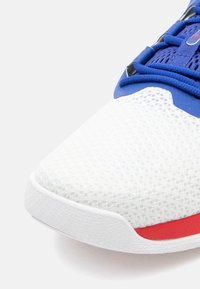 Sportchoenen met een witte mesh bovenkant, blauwe accenten en een rode streep op de zool. Heeft een gestructureerde afwerking en een gepolsterde tong.