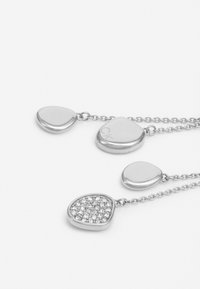 Srebrny naszyjnik z trzema gładkimi, zaokrąglonymi kształtami wisiorka; jeden z nich jest ozdobiony przezroczystymi kryształkami, tworząc dekoracyjny kontrast.