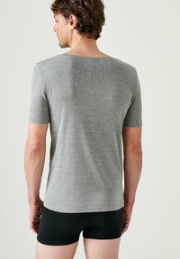 T-shirt grigia a maniche corte realizzata in tessuto morbido, con vestibilità rilassata e scollatura rotonda. Indossata con pantaloni corti neri.