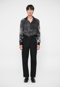 Zwarte satijnen shirt met een gestructureerd patroon, gecombineerd met zwarte gestructureerde broek en zwarte schoenen. De look is monochromatisch en gestroomlijnd.