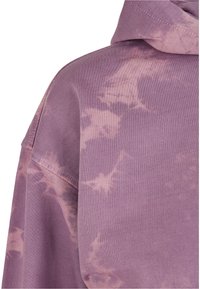 Fialová mikina s tie-dye dizajnom, vyrobená z mäkkej bavlnenej látky, s voľným strihom a kapucňou, ktorá má jemné svetlé vzory a švy.