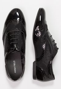 Chaussures derbies en cuir verni noir et mesh, à lacets et talons bas, présentées en vue de dessus et de côté sur fond blanc.