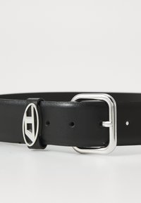 Ceinture en cuir noir avec une boucle rectangulaire en argent ornée d'une conception en ovale. Texture lisse, avec des trous pour l'ajustement.