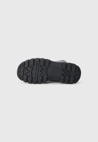 Semelle de chaussure en caoutchouc texturé noir avec des motifs de semelle profonds et un logo en relief. Forme légèrement courbée pour le confort et l'adhérence.