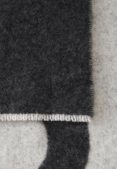 Gros plan d'une écharpe en laine gris foncé avec des franges sur un fond en tissu gris clair.