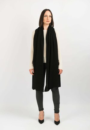 Black scarf draped around the neck, paired with a cream sweater and gray skinny jeans. The model wears black pointed-toe heels.