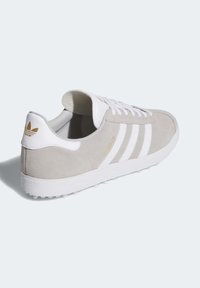 Szare zamszowe sneakersy z białymi paskami i sznurówkami. Biała gumowa podeszwa z teksturowanym uchwytem. Złoty detal logo na pięcie. Klasyczny sportowy design.