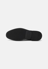Schwarze Gummisohle mit strukturierten Griffmustern. Verfügt über eine glatte Kante und einen intakten Branding-Bereich. Flaches Design, minimalistischer Stil.