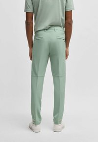 Jasnozielone elastyczne spodnie o gładkiej fakturze, z dwiema tylnymi kieszeniami i detalem logo. W połączeniu z białymi trampkami, widok z tyłu.