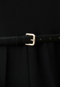 Cinturón de cuero negro con una hebilla de metal dorado, que cuenta con agujeros ajustables y una textura suave, estilizado sobre un fondo de tela negra.