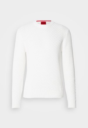 Bijeli pleteni pulover s teksturiranim uzorkom saća, rebrastim manžetama i rubom, s crvenom etiketom na izrezu.