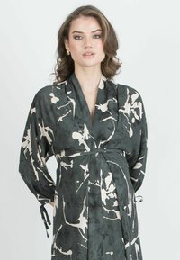 Dunkelgrünes Kimono-Kleid im Stil mit abstrakten cremefarbenen Mustern, weit geschnittenen Ärmeln, einem taillierten Gürtel und weichem, fließendem Stoff.