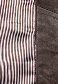 Hnědá kůže na pravé straně, hladká textura; pruhovaná látka v hnědé a bílé barvě na levé straně, jemný lesk, svislé linky.