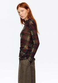 Dopasowany top z długim rękawem w przezroczysty wzór w kratę, zawierający ciemnozielone, czerwone i czarne kolory. Gładka tekstura z wysokim dekoltem.