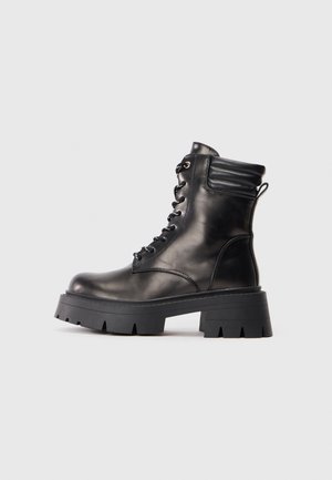 Zwarte leren enkelboots met ronde neus, dikke rubberen zool, vetersluiting aan de voorkant, gevoerd kraagje en lus aan de hiel.