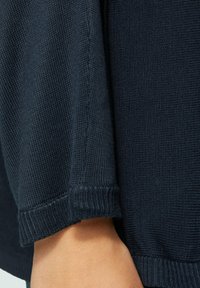 Ciemnoniebieski sweter wykonany z dzianiny o teksturowanym wykończeniu, z prążkowanymi mankietami i dołami. Zbliżenie podkreśla szczegóły tkaniny i szwów.
