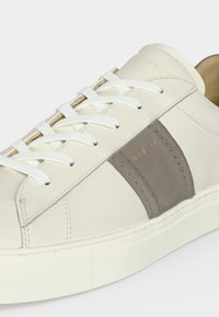Baskets en cuir blanc avec bande latérale grise, lacets blancs et logo doré discret "Rubik" sur le panneau latéral.