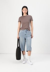 Camiseta marrón ajustada, culottes de mezclilla azul claro, zapatillas blancas y un bolso negro. Tejido suave, corte casual y jeans de corte relajado.
