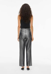 Pantalones de pierna ancha de color plata metálico con una textura suave, que cuentan con bolsillos traseros y una cintura alta, combinados con una camiseta ajustada negra.