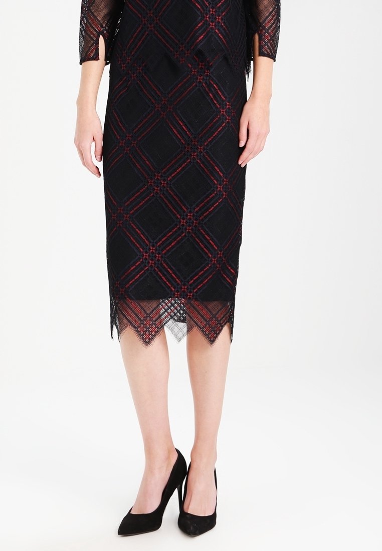 Svart spetsklänning med röda och marinblå geometriska mönster, figursydd silhuett, vågig nederkant och trekvartslånga ärmar. Kombinerad med svarta klackar.