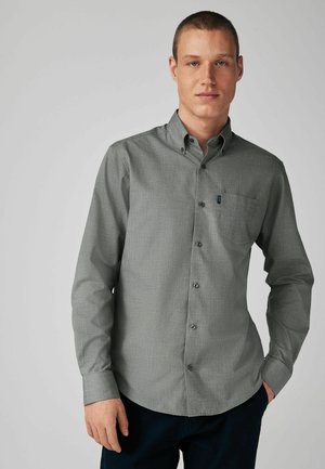 Camisa gris de botones con tela texturizada, mangas largas, cuello y un bolsillo en el pecho. Presenta botones oscuros y un patrón sutil.