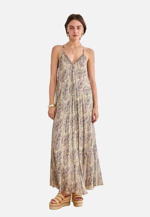 Mujer con un vestido maxi sin mangas de estampado cachemira, con tirantes finos, combinado con sandalias de plataforma y joyas doradas.