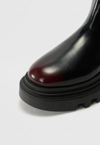 Stivaletto in pelle nera e bordeaux con punta arrotondata, suola in gomma nera testurizzata e delicati dettagli di cucitura alla base.