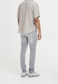 Chemise à manches courtes à carreaux beige clair, associée à un jean slim gris clair. Les chaussures sont gris clair avec des accents blancs.