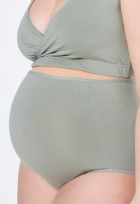 Světle zelený těhotenský top a vysoké kalhotky vyrobené z měkké, elastické tkaniny. Top má křížový design a bezšvové okraje.