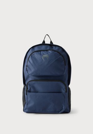 Sac à dos bleu marine avec deux poches avant zippées, une petite poignée noire en boucle en haut, et des poches latérales en mesh sur fond blanc.