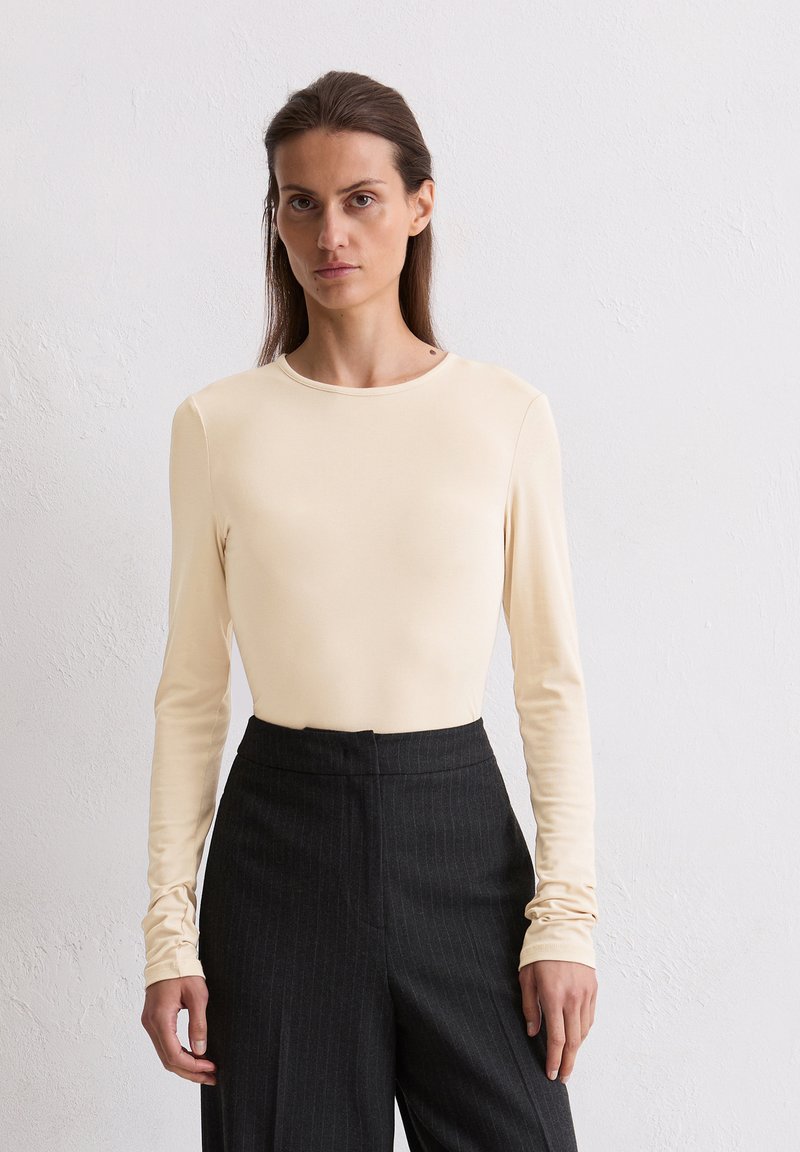 Langarmig, crèmekleurig top van soepel, rekbaar materiaal. Ronde hals, aansluitend ontwerp, gecombineerd met hoge taille streepjesslacks.