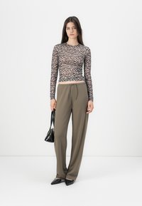 Langarmtop met een zwart en beige zebra patroon, gecombineerd met losse olijfgroene broeken en zwarte puntige flats, met een kleine zwarte tas.