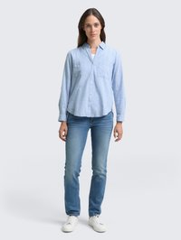 Lyseblå skjorte med krage og to brystlommer, parret med tettsittende blå jeans og hvite sneakers. Glatt stoff og avslappet design.