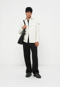 Camicia bianca a bottoni con tasca, abbinata a pantaloni larghi neri e sneakers nere. Gli accessori includono una borsa a tracolla nera.