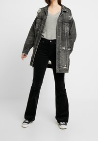 Överdimensionerad svart denimjacka med slitna detaljer, i kombination med en grå tröja och svarta utsvängda jeans, kompletterat med svarta sneakers.