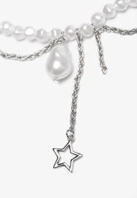 Collana di perle con accenti in catena d'argento; presenta una perla a forma di pera e un ciondolo a forma di stella. Colore bianco lucido e texture liscia.