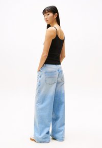 Light blue wide-leg jeans with a textured denim finish and two back pockets, paired with a fitted black tank top featuring thin straps.
