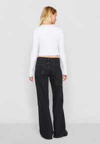 White long-sleeve crop top paired with high-waisted, wide-leg black jeans featuring a distressed detail and a black leather patch at the waist.