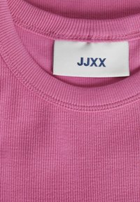 Rosa ribbad tyg t-shirt, med rund halsringning och en etikett med "JJXX" tryckt i marinblått. Mjuk textur med synliga sömmar.