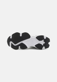 Sole di sneaker in bianco e nero con una superficie testurizzata, caratterizzata da un motivo di battistrada distintivo e un logo impresso sulla suola centrale.