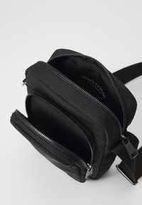 Borsa a tracolla nera in tessuto con due scomparti con cerniera, texture trapuntata, tracolla regolabile e logo visibile all'interno della tasca principale.